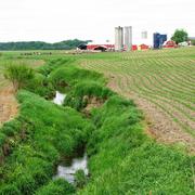 Agricultural Stream in Indiana in foreground with barn and silos in background
