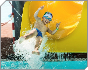 Boy giving two thumbs up as he flies off the end of a yellow waterslide in a big splash of water.