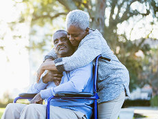A mature woman hugging her wheelchair-bound husband.
