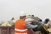 Back view of man putting bags of garbage into dumpster