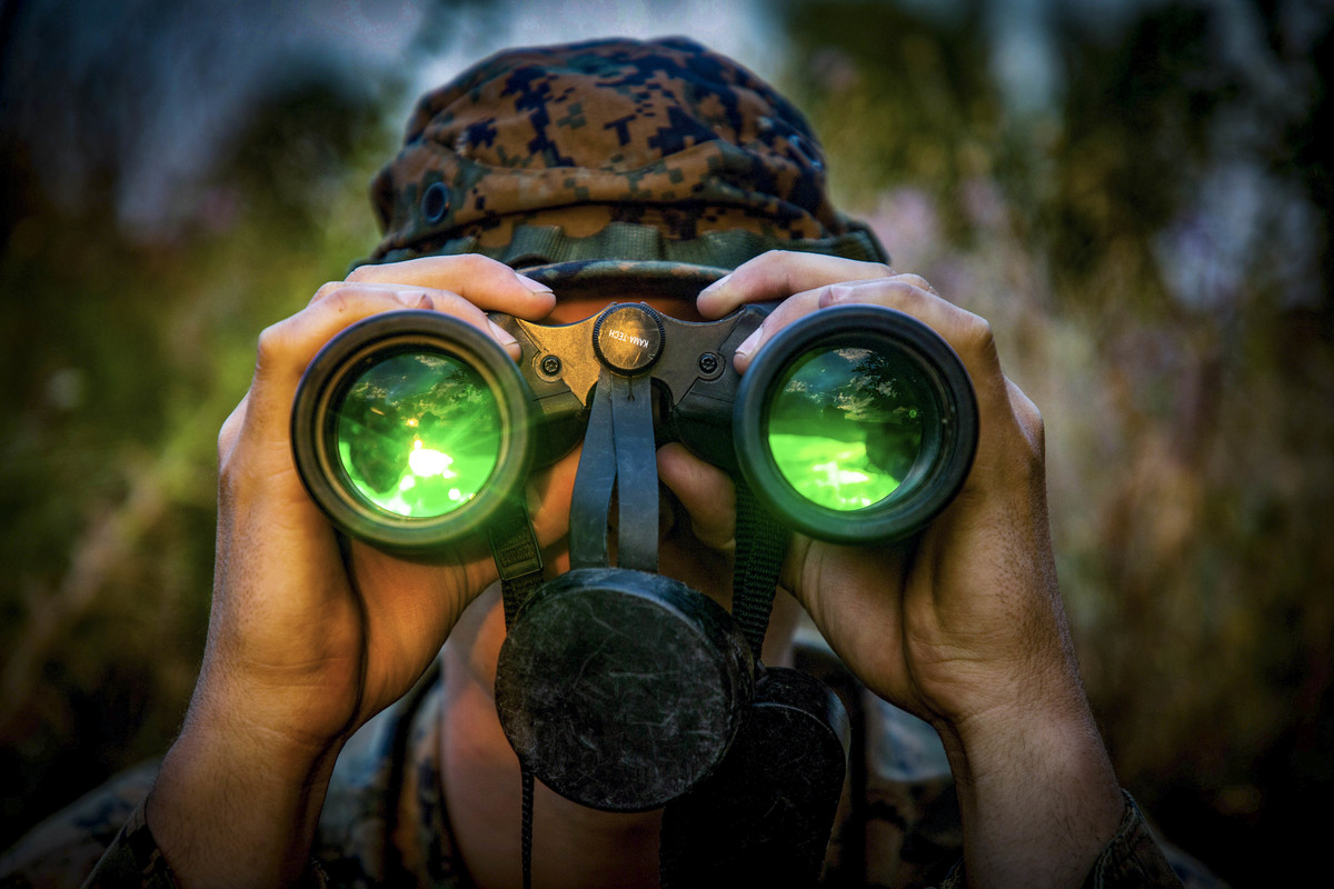A Marine looks through binoculars with green lenses.