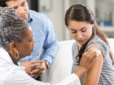 A teenage girl receiving a vaccine from a nurse.