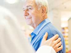 A doctor puts his hand on an older man's shoulder.