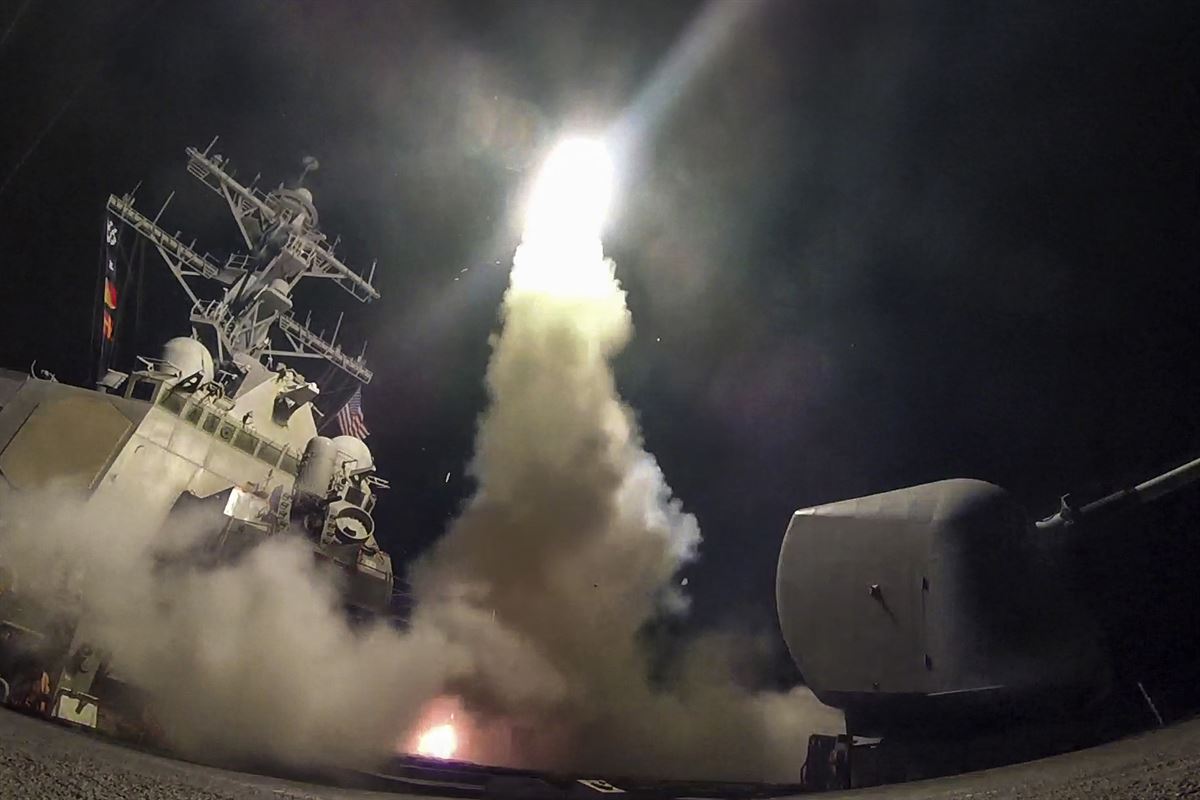 A destroyer launches a missile at night, creating smoke and light.