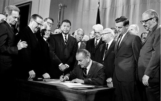 [El presidente Lyndon Johnson firma la Ley de Vivienda Justa junto con los copatrocinadores de la ley, senadores Edward Brooke (izquierda) y Walter Mondale (derecha)]