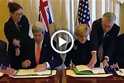 Screen capture of Kerry and Australian official signing a pact.