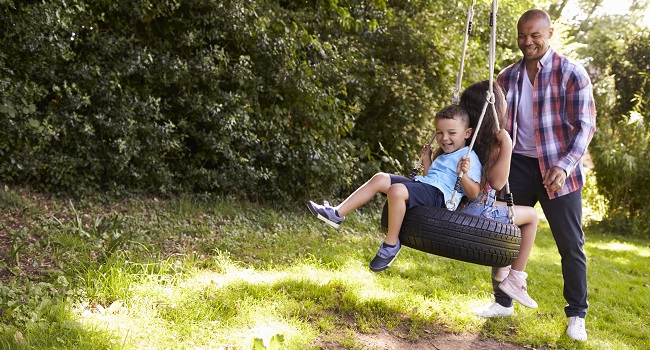 father pushing children on tire swing