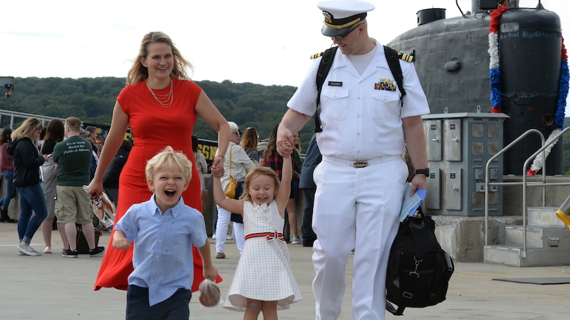 A sailor walks with a woman and two laughing kids.