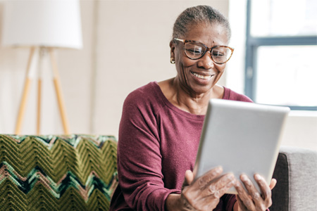 older woman smiling at the screen of the tablet she’s holding