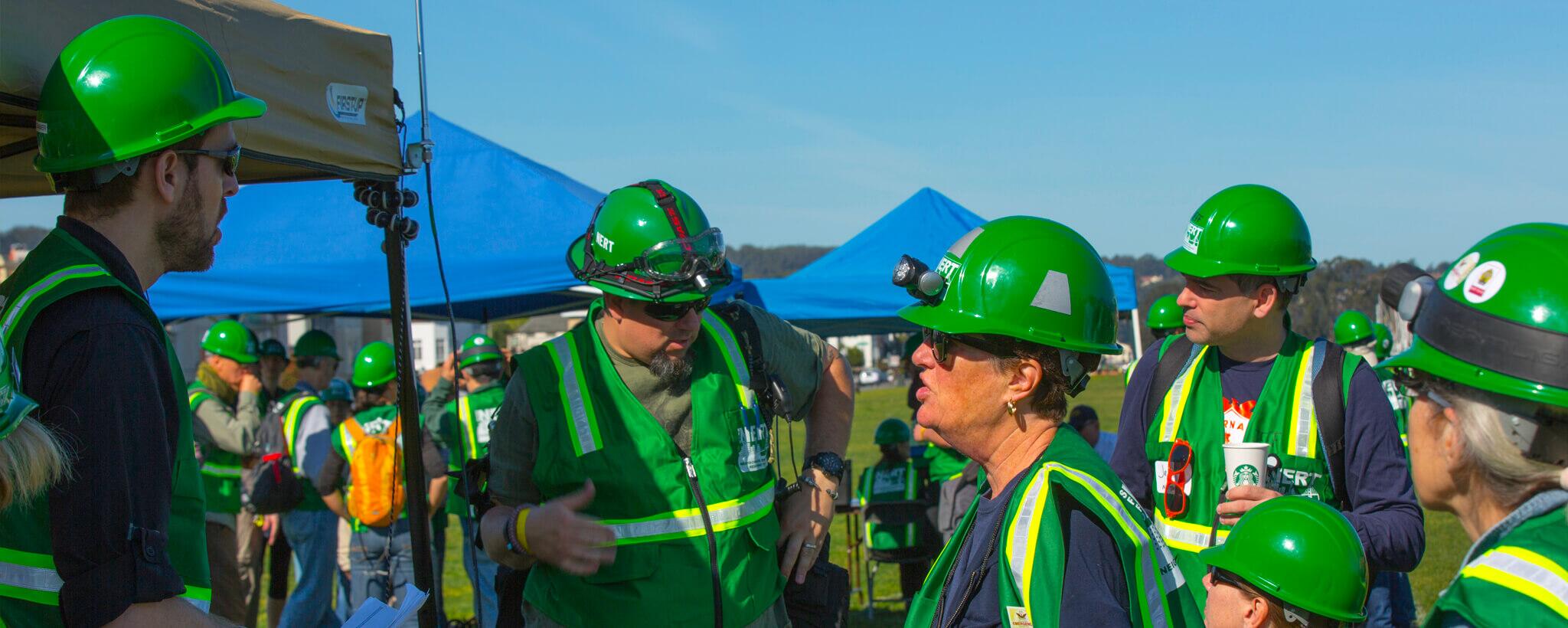 A group of men and women with green hard-hats and vests.