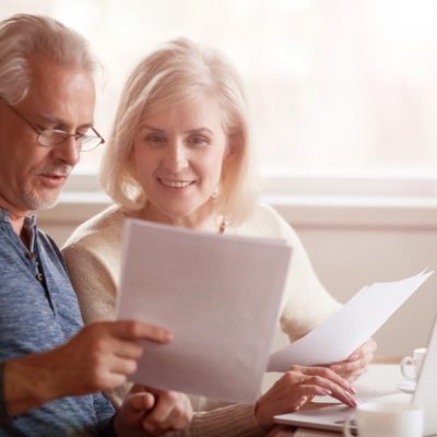 An older couple looking at documents while using a laptop