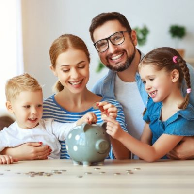 A family smiling while putting loose change into a piggy bank
