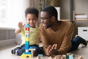 Happy cute little son playing game with dad building constructor tower from multicolored wooden blocks