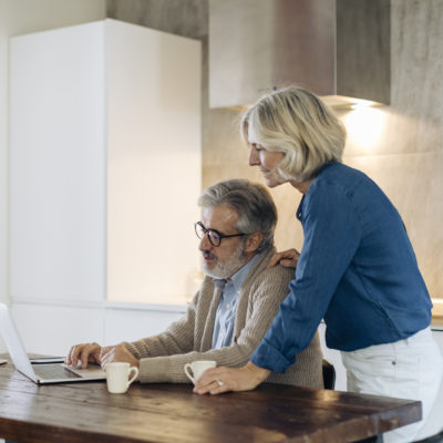 An elderly couple using a laptop while sitting at the kitchen table