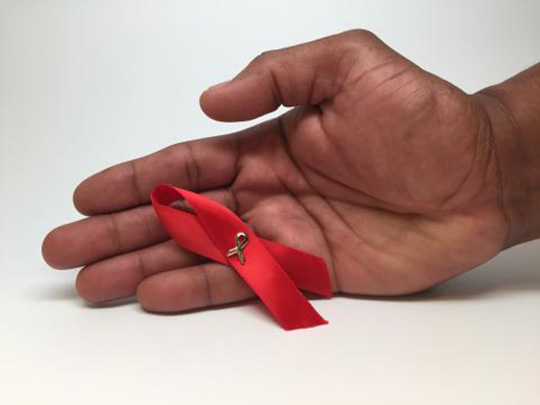  A man’s hand holding an HIV awareness ribbon. 