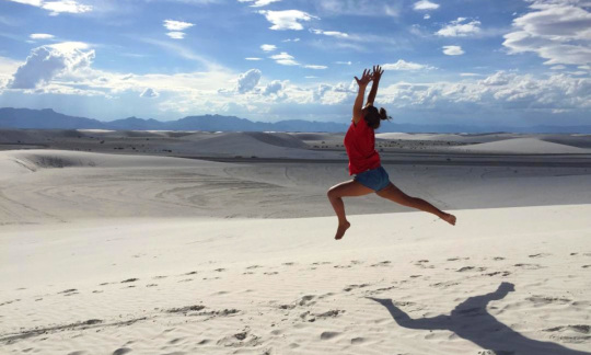 A woman leaping in the air as she dances across a landscape of white sand dunes.