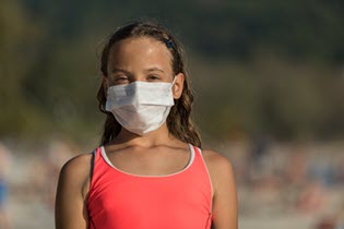 a young girl in a swimsuit wearing a mask on a beach