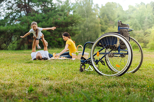 wheelchair in park, people in background playing