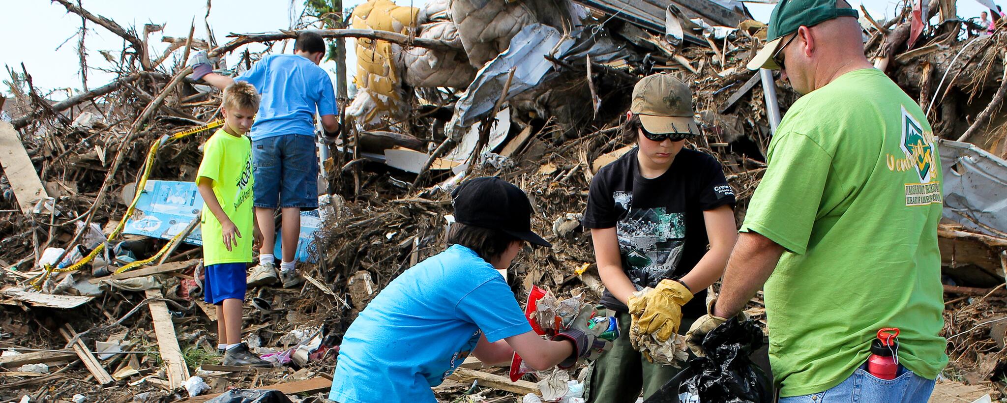 Niños exploradores y su líder recogiendo escombros de sus casas destrozadas