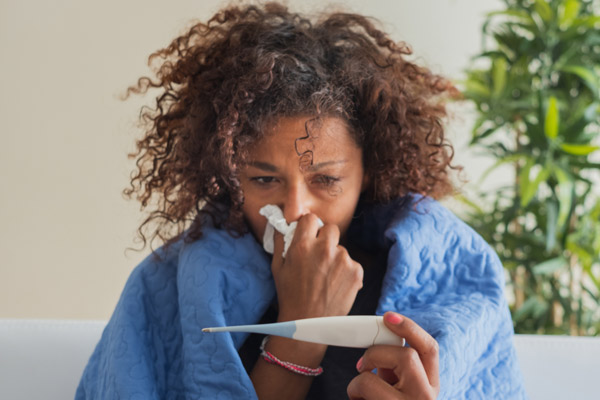 woman sneezing into kleenex and looking at thermometer