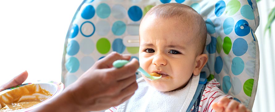Baby in highchair reacts negatively to baby food
