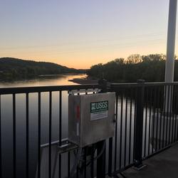 Streamgage mounted to bridge, view facing downstream river at dusk