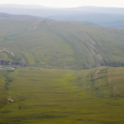 Image is an aerial shot showing grass-covered rolling hills with occasional exposed rock formations
