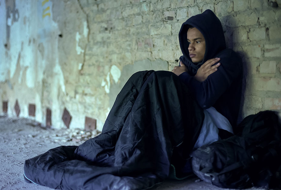 Homeless man against brick wall under hoodie and blanket