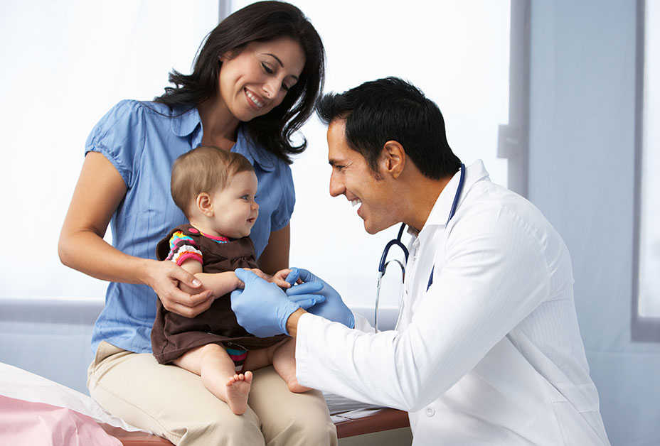 Doctor examining child on mother's lap and smiling