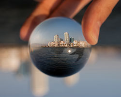 A hand holds a glass sphere with an inverted cityscape in its reflection