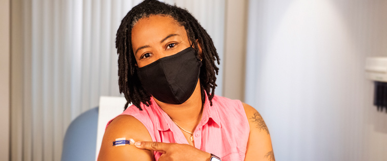 Woman wearing mask pointing to band aid on arm where she was vaccinated