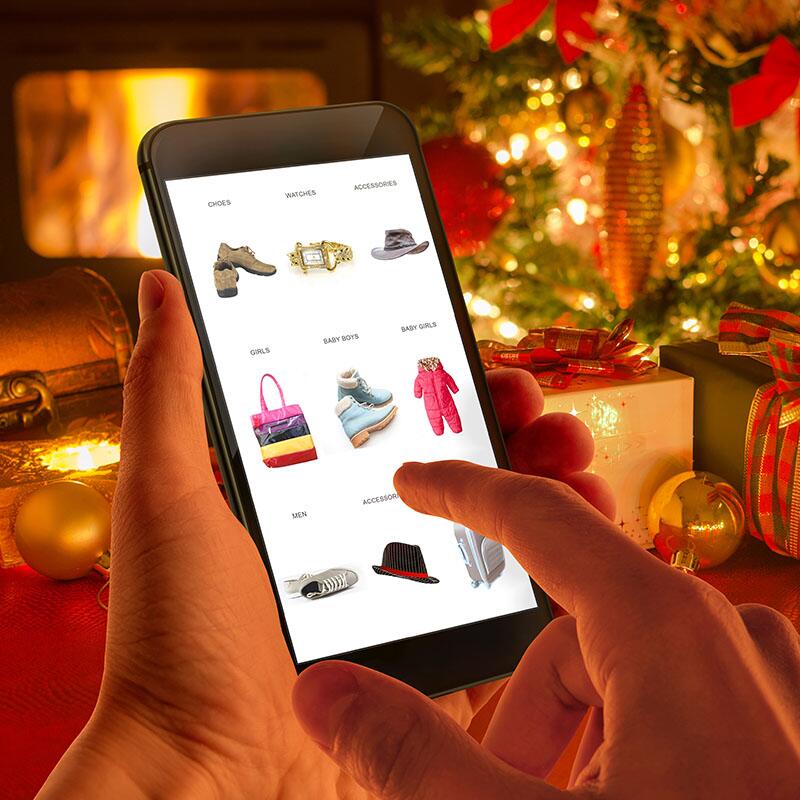 Hand buying clothes on a smart phone with holiday decorations inthe background
