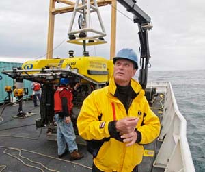 Dr. Robert Ballard stands on the deck of the NOAA research vessel Ronald H. Brown on May 31 and notes the threatening sky just prior to launching the Hercules ROV (background). Swells approaching 12 feet in height hampered launch and recovery maneuvers. Please credit NOAA / Bert Fox  National Geographic Society or NOAA?NG.