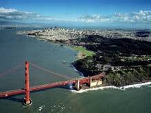 Aerial view of the Presidio looking eastward across the Golden Gate Bridge, bounded by the San Francisco bay on the left and the city of San Francisco in the background.