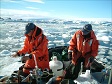 Two people stand in a motorized raft and move through sea ice. 