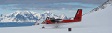 A red and white airplane on snow with mountains in the background.