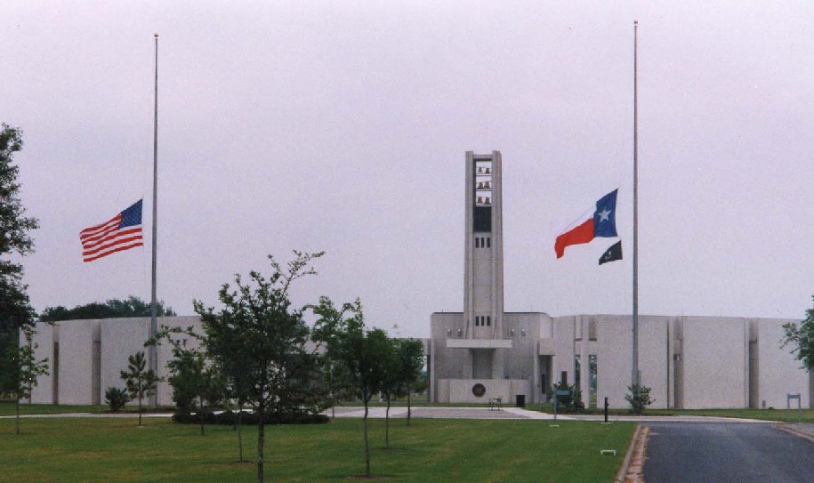 A picture of Houston's National Cemetery "Hemicycle". A 75-foot bell tower is also shown along with three flagpoles which flys the American, Texas, and City of Houston flags at half staff.