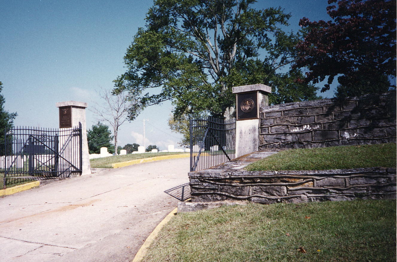 A photo of a road leading to an opened entrance gate with upright markers in the distance.