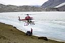 A helicopter hovers over the shore of an ice covered lake.