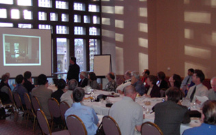 photo: Attendees meeting around a conference table, viewing a presentation