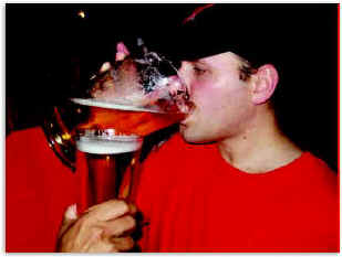 A young man guzzles beer from a pitcher.