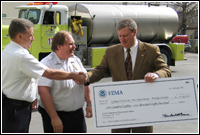 FEMA Region IX Regional Director Jeff Griffin presents the Reno Fire Department with a check to go toward a firefighting vehicle like the one in the background. FEMA News John Shea.