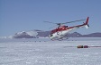 A helicopter lifts off from a snow-covered surface.