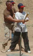 Master Sgt. Chris Cortazzo from the 416th Civil Affairs Battalion teaches an Iraqi youth to swing a bat to hit a baseball.
