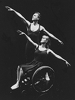 Female wheelchair dancer and male partner behind, both facing right with arms lifted upwards and to the right