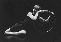 Female dancer on her side cradling a wheelchair wheel