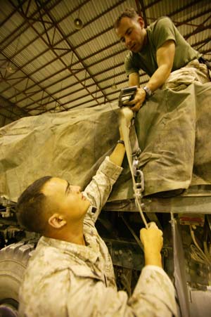 Cpl. Dimitri Petrenko, top, and Lance Cpl. Jesse W. Carpenter tighten a cargo strap during a weapons pickup at Abu Ghraib Warehouse Oct. 10, 2004. Marines with CSSC-115 delivered more than 18,500 weapons, ammunition and supplies to the Ramadi Police Academy Oct. 11, 2004. The Ramadi Police Academy will use the weapons, ammunition and supplies for training their recruits in handcuffing procedures and weapons familiarization. CSSC-115, part of the 1st Force Service Support Group, directly supports Marines operating in hotspots like Fallujah and Ramadi. The 1st FSSG is responsible for providing logistical support, such as food, ammunition and medical supplies, to all Marine forces operating in Iraq. Petrenko is a 24-year-old native of Queens, N.Y., and Carpenter is a 24-year-old Martinez, Calif., native. Photo by: Sgt. Luis R. Agostini