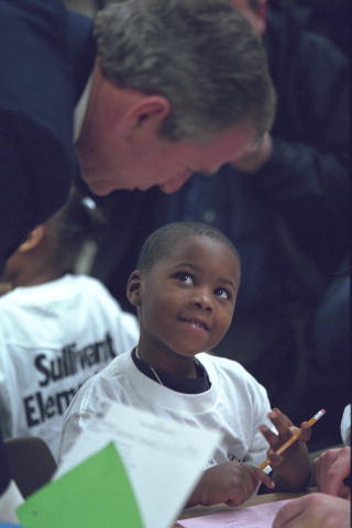President Bush helps a young male African-American student read.