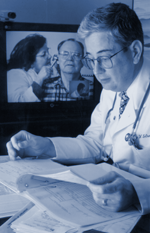 Physician looking at charts with TV monitor in background.