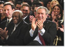 President George W. Bush applauds during the Celebration of Hispanic Heritage Month in the East Room, Thursday, Oct 2, 2003. Also pictured from left are, Tony Garza, U.S. Ambassador to Mexico and Pedro Knight, the husband of late singer Celia Cruz. White House photo by Eric Draper.